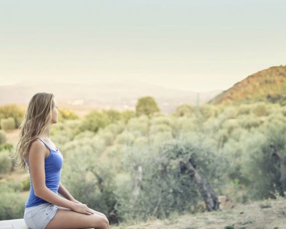 A woman in casual attire sits peacefully, enjoying a scenic outdoor view of nature.